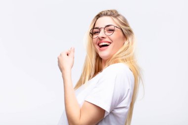 Genç, güzel sarışın kadın mutlu, pozitif ve başarılı hissediyor, meydan okumayla karşılaştığında motive oluyor veya beyaz duvara karşı iyi sonuçları kutluyor.