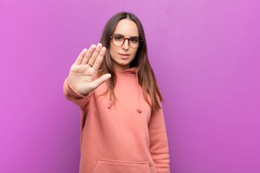 Genç ve güzel bir kadın ciddi, sert, hoşnutsuz ve kızgın görünüyor. Avuç içinin açık olması mor duvara karşı durmasını sağlıyor.