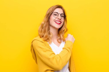 Genç, güzel sarışın kadın mutlu, pozitif ve başarılı hissediyor, meydan okumayla karşılaştığında motive oluyor veya sarı duvara karşı iyi sonuçları kutluyor.