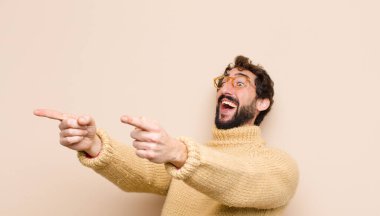 Genç havalı adam mutlu ve kendinden emin, kamerayı iki eliyle gösteriyor ve gülüyor, seni düz duvara karşı seçiyor.