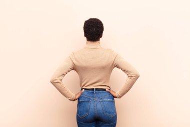 Genç, siyah bir kadının kafası karışmış ya da dolu ya da şüphe ve soru dolu, merak içinde, elleri kalçasında, dikiz aynasından.