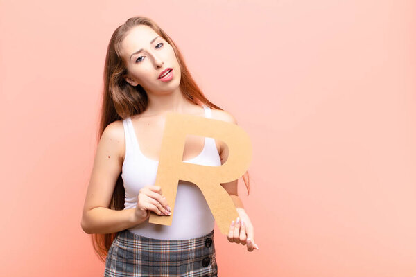 Блондинка смущенная, сомневающаяся, думающая, держа букву "R" в руках, чтобы образовать слово или предложение.