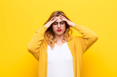 young pretty blonde woman looking stressed and frustrated, working under pressure with a headache and troubled with problems against yellow wall clipart