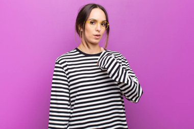 Kafası karışmış, kafası karışmış ve kendine güveni olmayan genç güzel bir kadın kendini gösterip kim olduğumu soruyor, ben mi? mor duvara yaslan