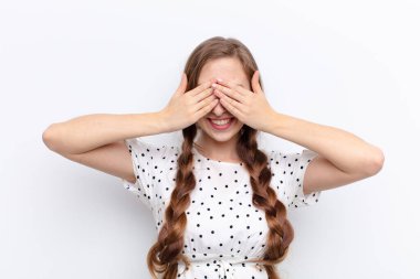 Genç sarışın kadın gülümsüyor ve mutlu hissediyor, iki eliyle gözlerini kapatıyor ve beyaz duvara karşı inanılmaz bir sürpriz bekliyor.