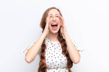 yound blonde woman feeling happy, excited and positive, giving a big shout out with hands next to mouth, calling out against white wall clipart