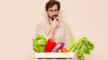 Yeşil bakkal, ciddi, düşünceli ve güvensiz görünüyor. Bir kolu çapraz, eli çenesinde, seçenekleri değerlendiriyor.