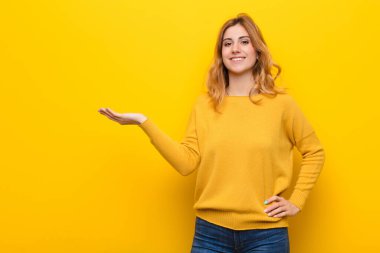 Genç, güzel sarışın kadın gülümsüyor, kendinden emin, başarılı ve mutlu hissediyor, fotokopi odasında sarı duvara karşı fikir veya konsept gösteriyor.