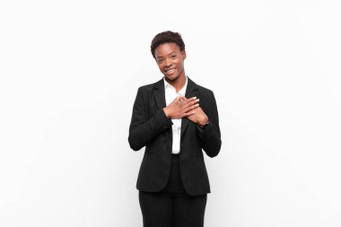 Genç siyah kadın romantik, mutlu ve aşık, neşeyle gülümsüyor ve beyaz duvara karşı kalbe yakın el ele tutuşuyor.