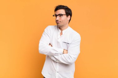 Genç yakışıklı adam omuz silkiyor, kafası karışık ve kararsız, kolları bağlı ve şaşkın görünüyor.