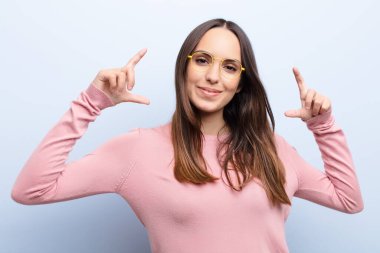 Genç, güzel bir kadın iki eliyle kendi gülümsemesini çiziyor, olumlu ve mutlu görünüyor, mavi duvara karşı sağIık kavramı.