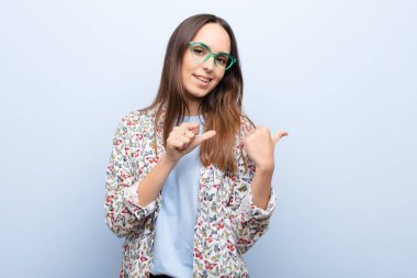 Genç, güzel bir kadın neşeyle gülümsüyor ve yan taraftaki fotokopi alanını işaret ediyor. Mavi duvara karşı mutlu ve tatmin olmuş hissediyor.