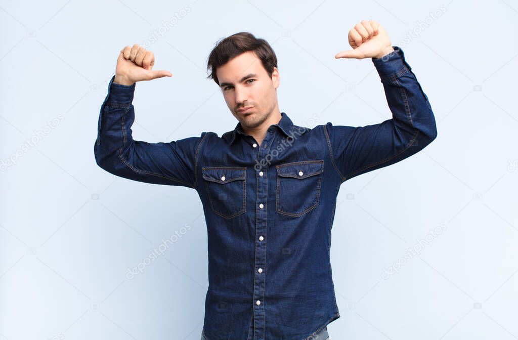 young handsome man feeling proud, arrogant and confident, looking satisfied and successful, pointing to self against blue wall