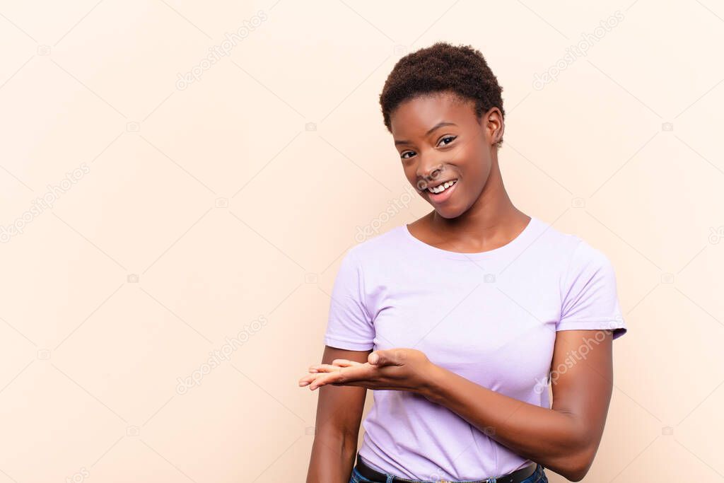 young pretty black womansmiling cheerfully, feeling happy and showing a concept in copy space with palm of hand