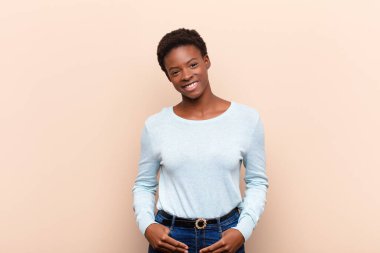 Genç ve güzel siyahi kadın neşeli ve tesadüfen gülümsüyor pozitif, mutlu, kendinden emin ve rahat bir ifadeyle