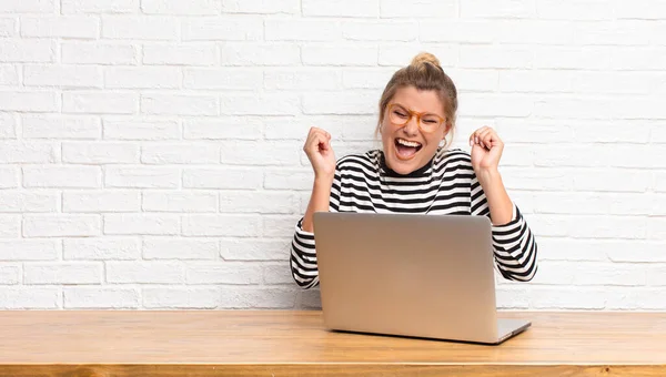 young pretty latin woman looking extremely happy and surprised, celebrating success, shouting and jumping sitting with her laptop