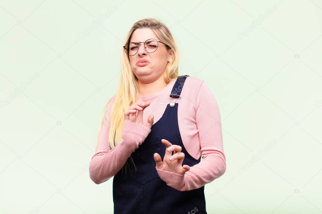 young pretty blonde woman feeling disgusted and nauseous, backing away from something nasty, smelly or stinky, saying yuck against flat wall