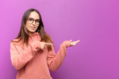Genç, güzel bir kadın gülümsüyor, mutlu, kaygısız ve tatmin olmuş hissediyor. Mor duvara karşı fotokopi alanındaki konsepte ya da fikre işaret ediyor.