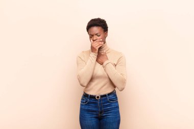 Boğazı ağrıyan ve grip belirtileri gösteren, ağzı kapalı öksüren genç, siyah bir kadın.