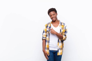 Genç, güzel, siyah kadın neşeyle gülümsüyor, mutlu hissediyor ve yan ve yukarı doğru işaret ediyor, kopya uzayda nesne gösteriyor.