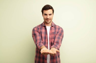 Genç yakışıklı adam mutlu bir şekilde gülümsüyor arkadaş canlısı, kendinden emin, olumlu bakışlı, bir nesne ya da konsept sunuyor ve gösteriyor.