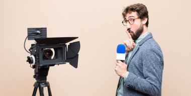 Televizyon sunucusu ciddi görünüyor ve parmaklarını dudaklarına bastırarak sessizlik ya da sessizlik talep ediyor, sır saklıyor.