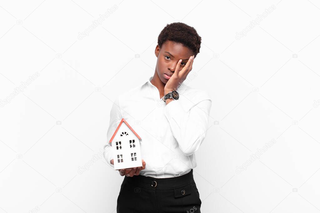 young pretty black womanfeeling bored, frustrated and sleepy after a tiresome, dull and tedious task, holding face with hand with a house model