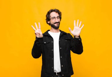 Genç ve yakışıklı adam gülümsüyor ve arkadaş canlısı görünüyor. Sekiz ya da sekiz numarayı gösteriyor. Elleri önde, turuncu duvara doğru sayıyor.