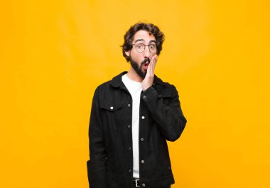 Genç çılgın yakışıklı adam şok olmuş ve hayrete düşmüş hissediyor. Ağzı açık halde turuncu duvara yaslanmış, yüz yüze inanamıyor.