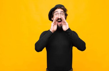 Genç Fransız ressam mutlu, heyecanlı ve pozitif hissediyor. Elleri ağızda, turuncu duvara karşı bağırıyor.