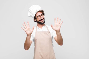 Genç ve çılgın şef gülümsüyor ve arkadaş canlısı görünüyor, onuncu ya da onuncu numarayı gösteriyor, eli önde, beyaz duvara doğru sayıyor.