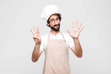 Genç çılgın şef gülümsüyor ve arkadaş canlısı görünüyor. Sekiz ya da sekiz numarayı gösteriyor. Elleri önde, beyaz duvara doğru sayıyor.