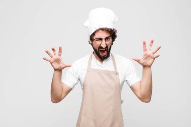 Genç çılgın şef panik ya da öfke içinde bağırıyor, şok olmuş, korkmuş ya da öfkeli, elleri beyaz duvara dayalı.