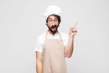 Genç çılgın şef bir fikri fark ettikten sonra mutlu ve heyecanlı bir dahi gibi hissediyor, neşeli bir şekilde parmağını kaldırıyor, eureka! Beyaz duvara yaslan