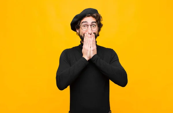 若いフランス人アーティストの男が驚いて手で口を覆いオレンジの壁に対して可愛い表情で笑い — ストック写真