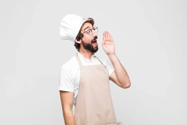 young crazy chef profile view, looking happy and excited, shouting and calling to copy space on the side against white wall