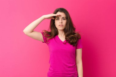 Genç ve güzel bir kadın, pembe duvara karşı saygı göstererek, onur ve vatanseverlik eylemiyle kameraya selam veriyor.