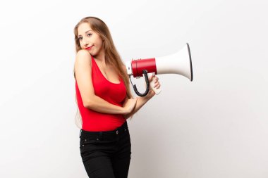 Genç sarışın kadın omuz silkiyor, kafası karışık ve kararsız, kolları çapraz ve şaşkın, elinde bir megafonla bakıyor.