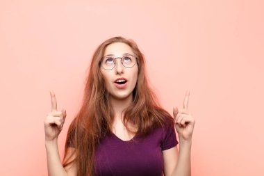 Genç sarışın kadın korkuyla ve ağzı açık bir şekilde şaşkın ve şaşkın bir bakışla yukarıya bakıyor.