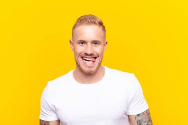 Genç sarışın yakışıklı, neşeli, kaygısız, asi tavırlı, şakacı ve dilsiz, sarı duvara karşı eğlenen