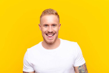 Genç sarışın yakışıklı, neşeli, kaygısız, asi tavırlı, şakacı ve dilsiz, sarı duvara karşı eğlenen