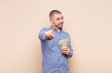 Genç yakışıklı adam gururla gülümsüyor ve gururla bir numaralı pozunu veriyor. Kendini dolar banknotları olan bir lider gibi hissediyor.