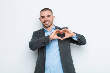 Genç işadamı gülümsüyor ve mutlu, sevimli, romantik ve aşık, iki elini de duvara dayayarak kalbi şekillendiriyor.