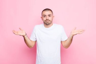 Genç yakışıklı adam şaşkın ve şaşkın, şüpheci, farklı seçenekleri tartıyor ya da seçiyor düz duvara karşı komik bir ifadeyle