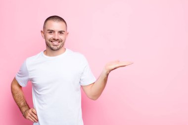 Genç yakışıklı adam gülümsüyor, kendinden emin, başarılı ve mutlu hissediyor, fotokopi odasında düz duvara karşı fikir veya konsept gösteriyor.