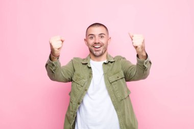 Genç ve yakışıklı bir adam inanılmaz bir başarıyı kutluyor. Kazanan gibi, heyecanlı ve mutlu görünüyor. Al bakalım! yassı duvara karşı