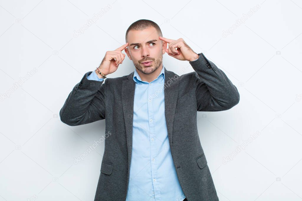 young businessman feeling confused or doubting, concentrating on an idea, thinking hard, looking to copy space on side against flat wall