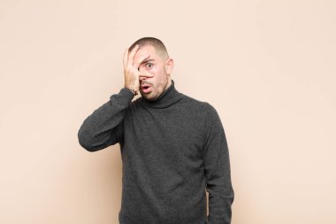 Genç yakışıklı adam şok olmuş, korkmuş ya da korkmuş görünüyor. Yüzü elle kaplanmış ve parmaklarının arasından düz duvara bakıyor.