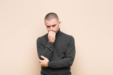 Genç yakışıklı adam ciddi, düşünceli ve endişeli, elleri çenesine yaslanmış bir şekilde duvara bakıyor.