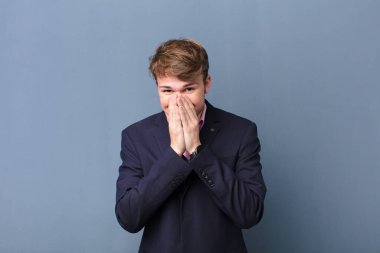 Genç sarışın adam mutlu, neşeli, şanslı ve şaşkın görünüyor. İki eli de duvara yaslanmış, ağzı kapalı.